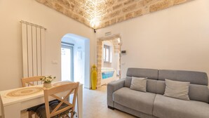 Una sala de estar moderna con un sofá gris, una mesa de comedor de madera con un mantel individual y una pared de piedra.