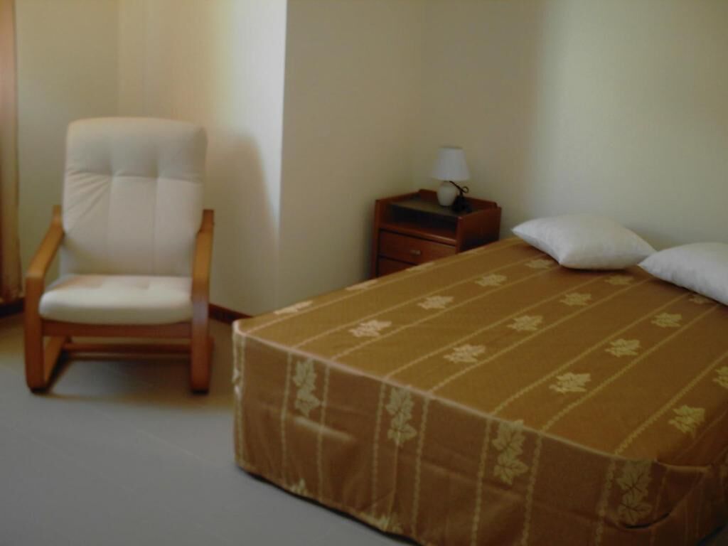 Un dormitorio con una cama, una silla, una mesita de noche con lámpara y una ventana en la pared.