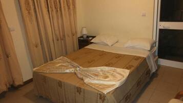 Una habitación de hotel con cama, cortinas, mesita de noche y ventana.