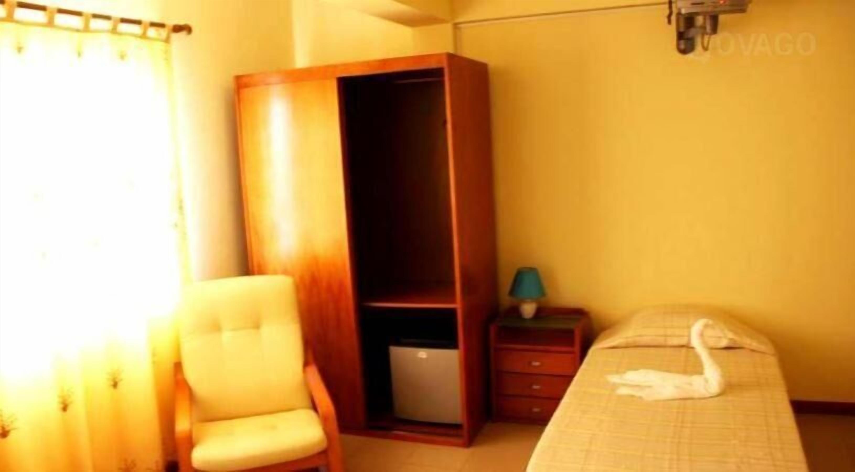 Un dormitorio con cama, una silla, armario, mesita de noche y lámpara.