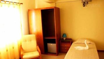 Un dormitorio con cama, una silla, armario, mesita de noche y lámpara.