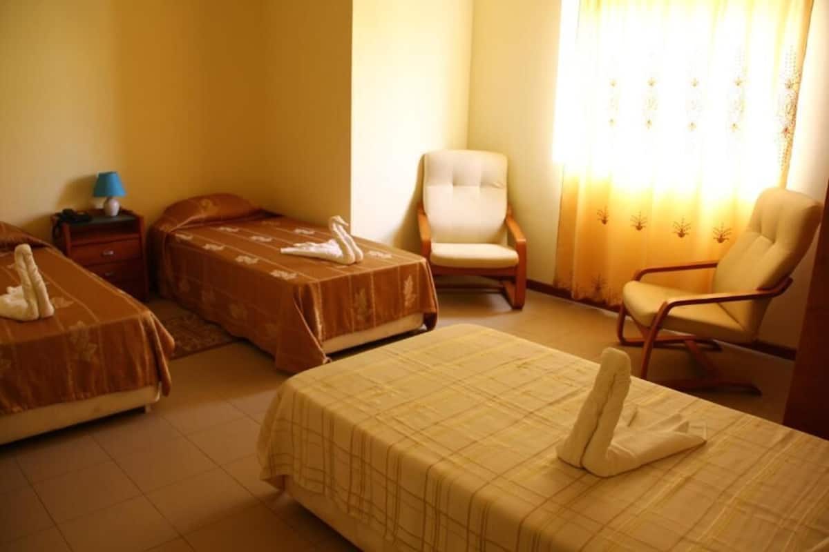 Habitación de hotel con dos camas, una silla y una mesita de noche con lámpara.