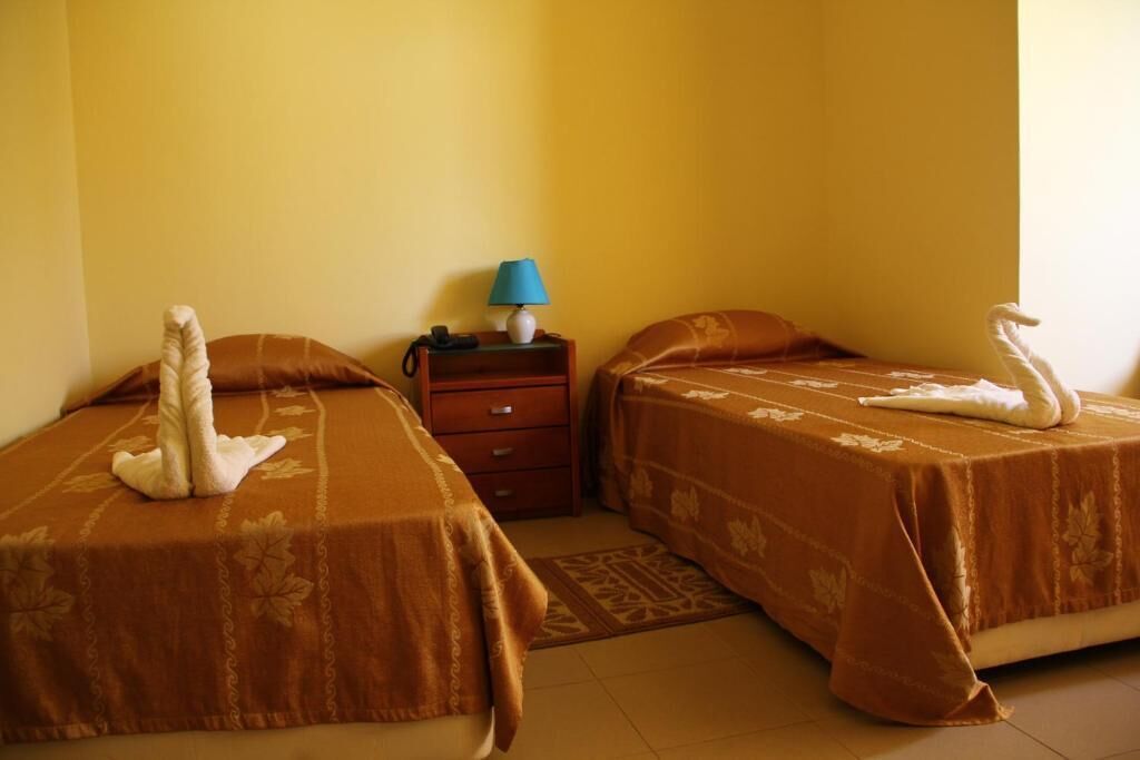 A hotel room with two beds, a nightstand with a lamp, and a telephone.