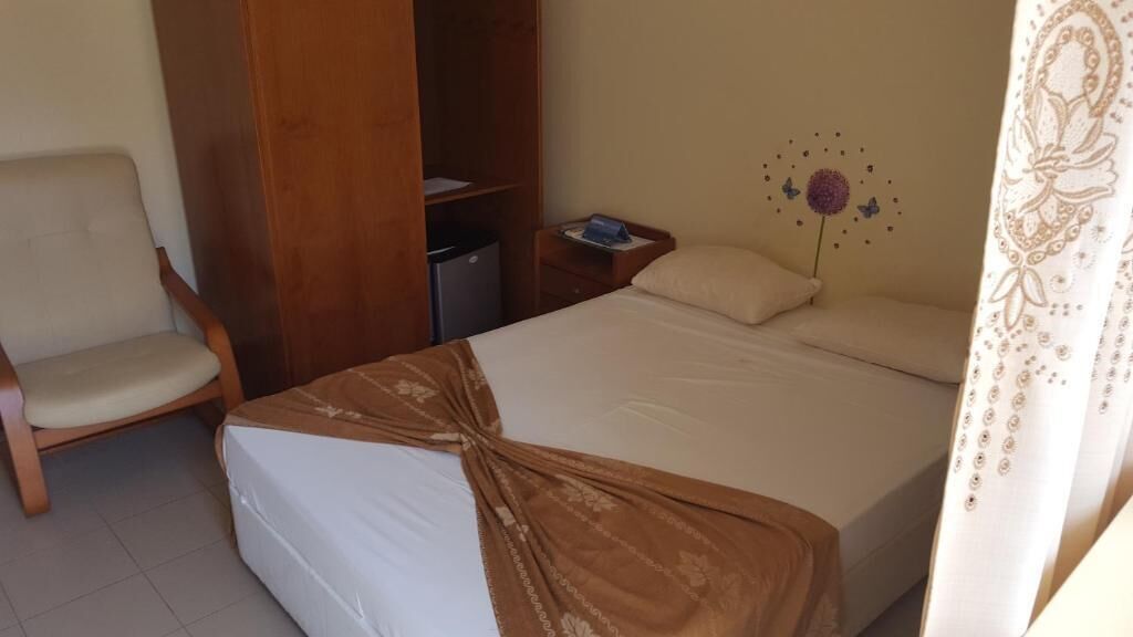 Una camera d'albergo con un letto, una sedia, un armadio, un comodino e un elemento decorativo a parete.
