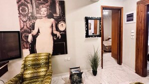 A living room with a large abstract painting, a television, a patterned armchair, and a small plant.