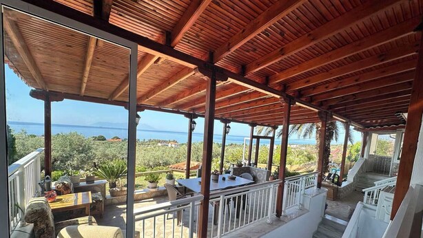 A covered outdoor seating area with a view of the sea and greenery.