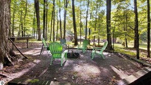 A forested campsite with a picnic table and four green chairs. - Relax & Recharge | Fire pit, Game Room, Near Torch Lake (Bellaire)