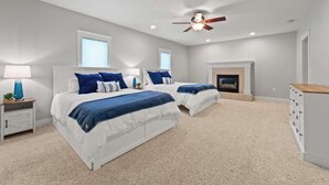 A bedroom with two beds, a ceiling fan, a fireplace, and a dresser. - Relax & Recharge | Fire pit, Game Room, Near Torch Lake (Bellaire)