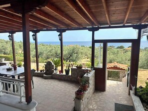 Une terrasse couverte avec vue sur la mer, comprenant une table agrémentée de plantes en pot, un banc et un sol carrelé.