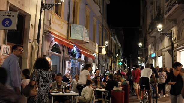 Une rue animée la nuit, où l’on voit des gens dîner dans des cafés en plein air.