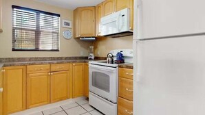 Una cucina con mobili in legno, un fornello bianco, un forno a microonde e un frigorifero.