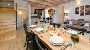 Un comedor con una mesa de madera dispuesta para cuatro, una cocina al fondo y una escalera que sube a otro nivel.