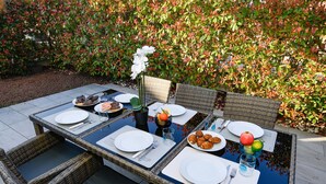 Un área de comedor al aire libre con sillas de mimbre, una mesa de vidrio y una variedad de comida y bebidas.