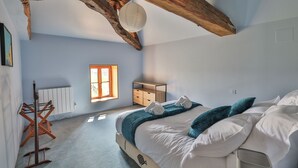 A bedroom with a wooden ceiling, a radiator, a wooden dresser, a bed with white bedding and teal pillows, and a window with sunlight. - Private estate with swimming pool, garden & open spaces - Up to 12 guests (Bréville)