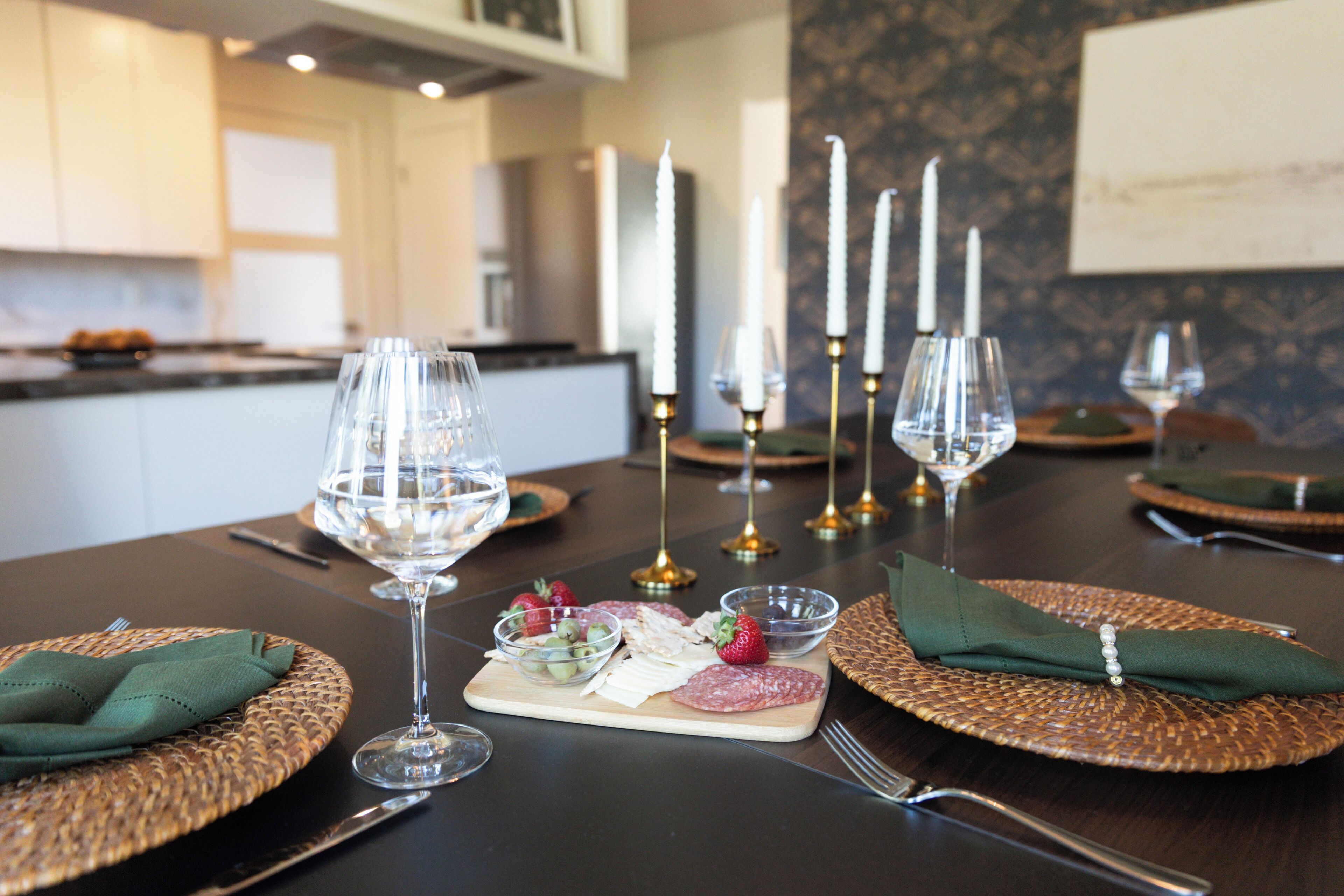 Mesa de comedor dispuesta con copas de vino, platos y un centro de mesa con velas.