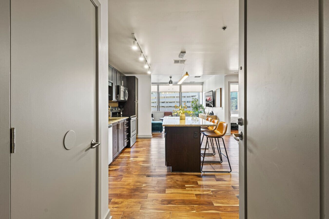 A modern kitchen with a central island, wooden flooring, and a view of the city through large windows.