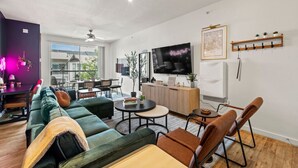 A modern living room with a green sofa, a dining table, and a TV mounted on the wall. - 2BR Modern Stay • Walk to AA Center• Free Parking (Dallas)