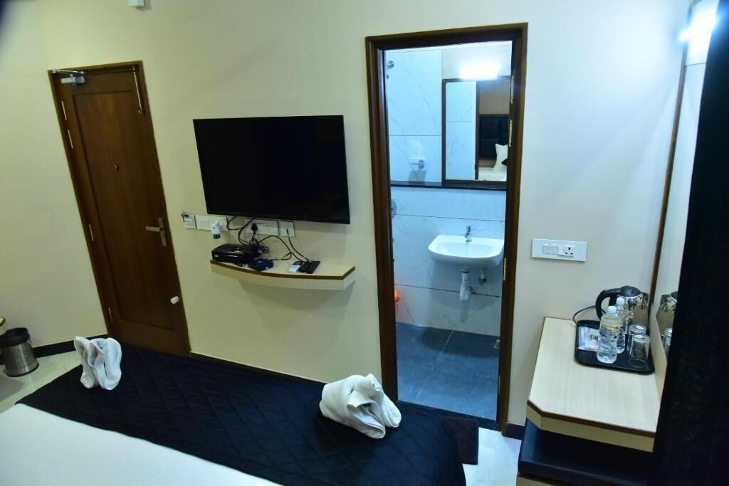 A hotel room with a bed, a TV mounted on the wall, a bathroom with a sink and mirror, and a small table with toiletries.
