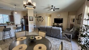 Ein modernes Wohnzimmer mit einem grauen Sofa, einem Esstisch mit Platzsets und einem Deckenventilator.