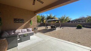 Ein überdachter Patio-Bereich mit Deckenventilator, einer Couch, einem Tisch und einem Gazebo.