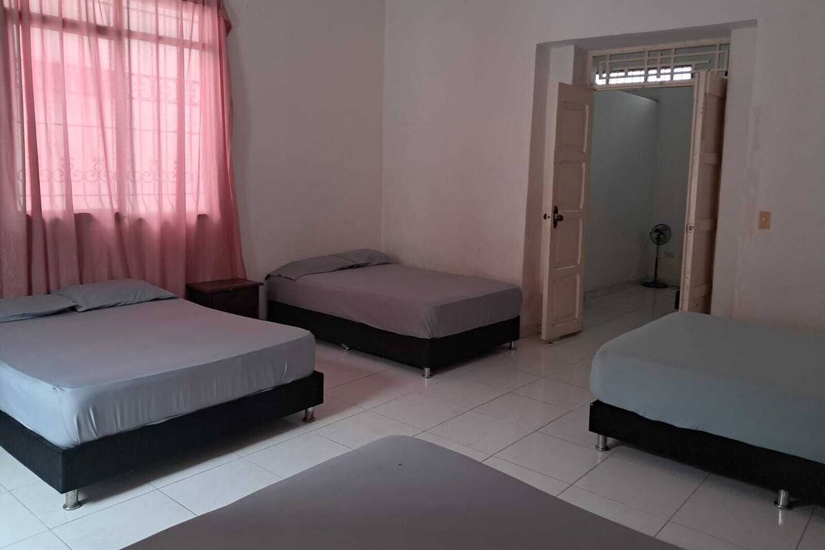 Una habitación con tres camas, una puerta que da a otra habitación y un ventilador en un rincón.