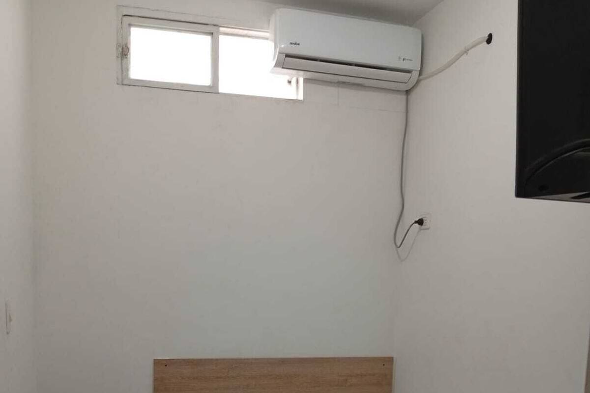 Habitación pequeña con cama individual, cabecera de madera, ventana y aire acondicionado instalado en la pared.