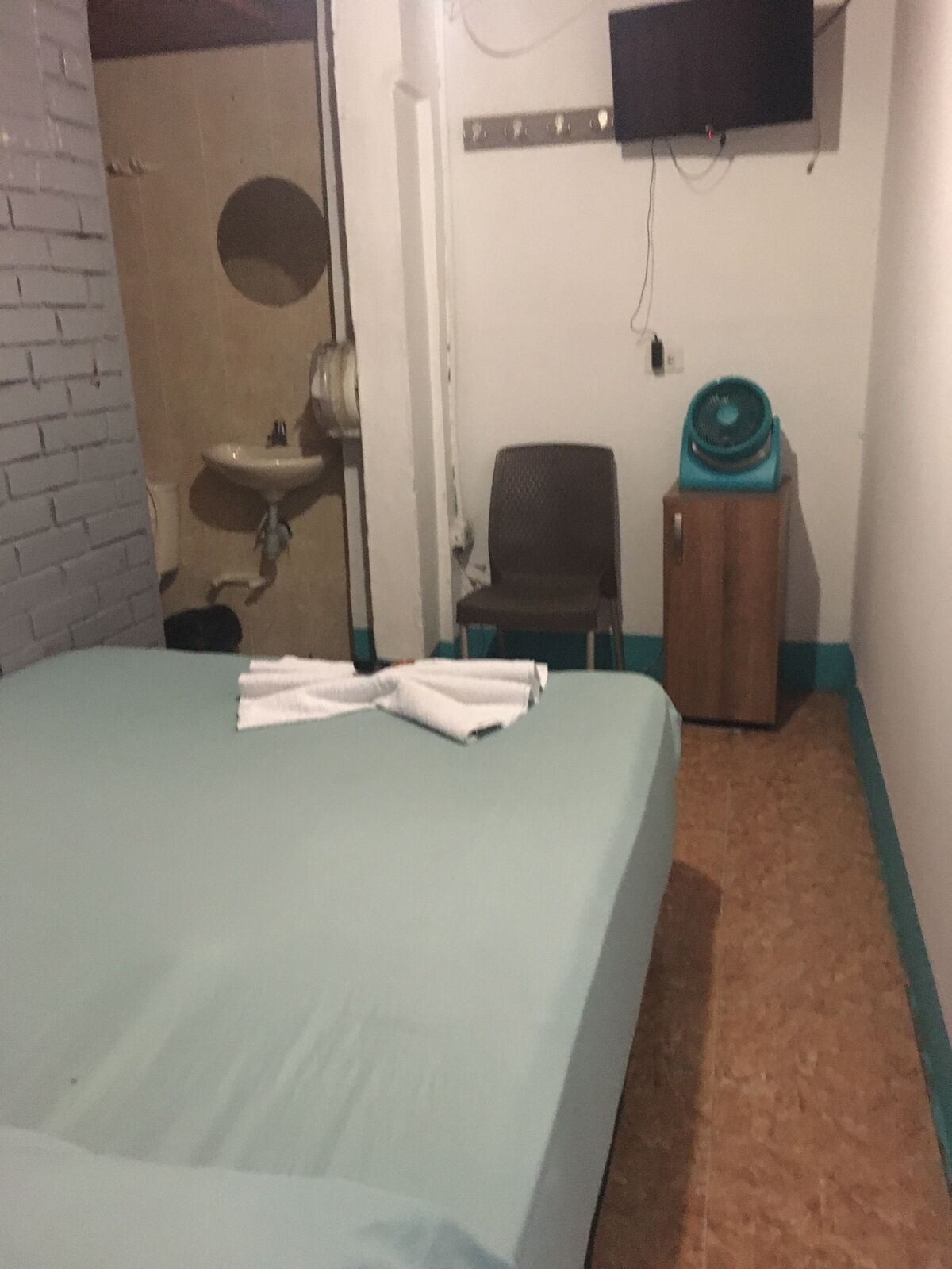A hotel room with a bed, a chair, a small table, a sink, and a television mounted on the wall.