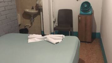 Habitación de hotel con cama, una silla, una mesita, un lavamanos y un televisor montado en la pared.