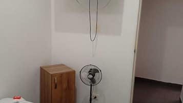 Una habitación con una cama, un televisor montado en la pared, un armario de madera y un ventilador de pie.
