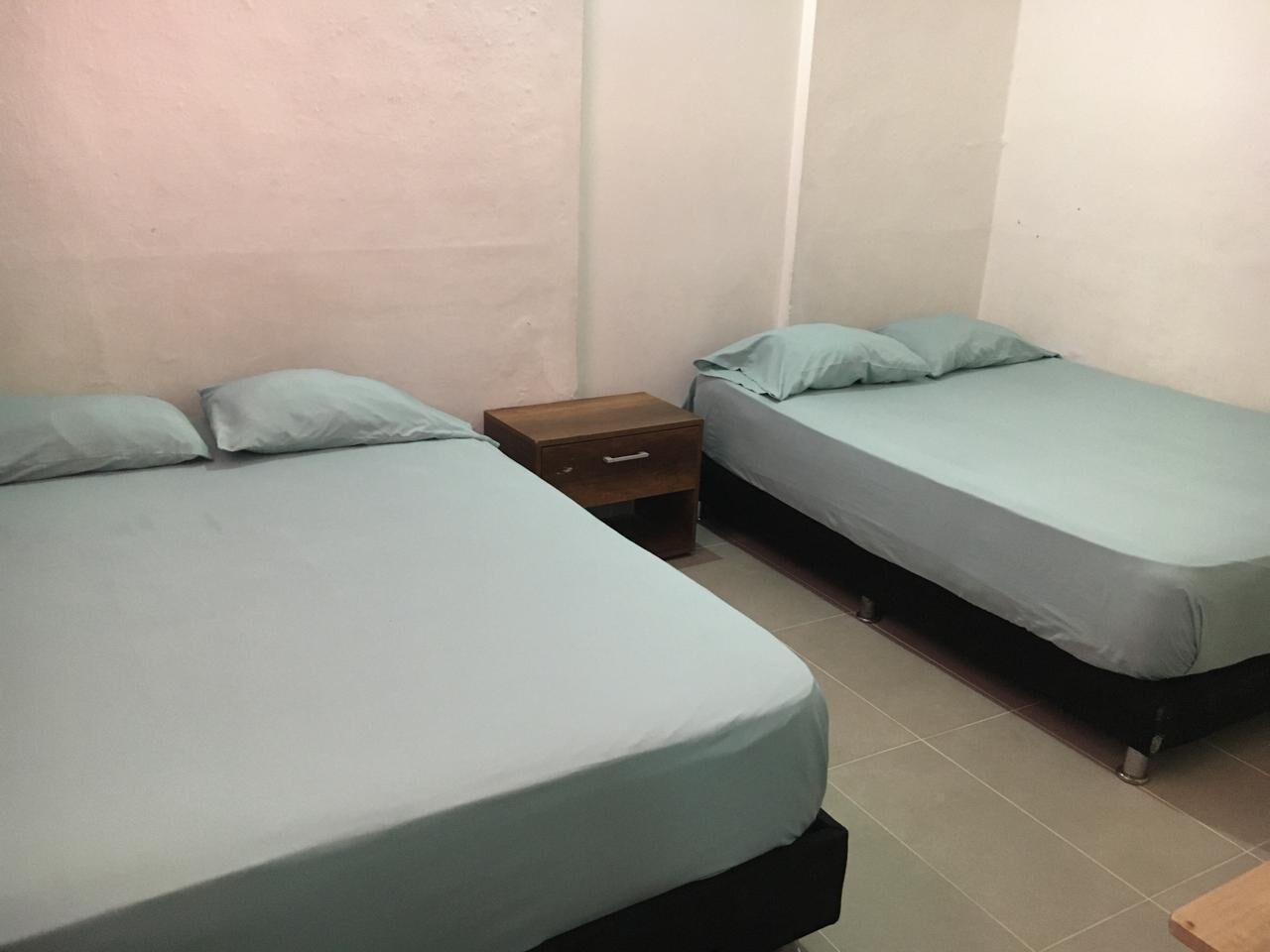Una habitación pequeña y limpia con dos camas individuales, cada una con una almohada y una mesita de noche de madera.