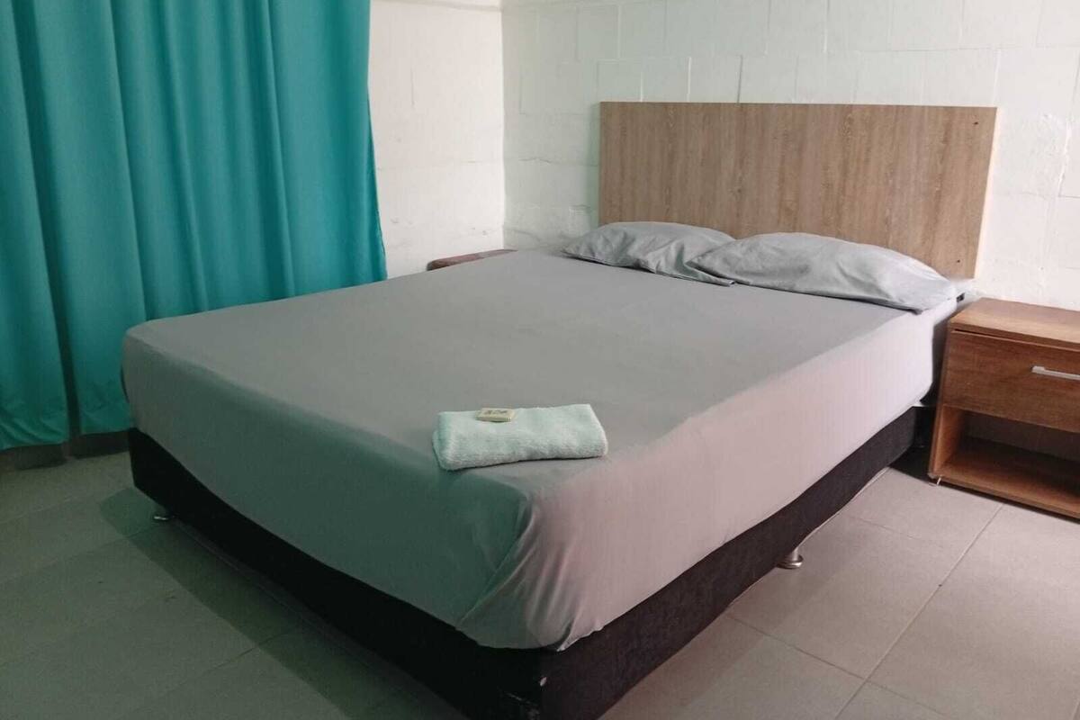 Una cama individual con cabecera de madera, una colcha gris y un cojín pequeño en el pie de cama.