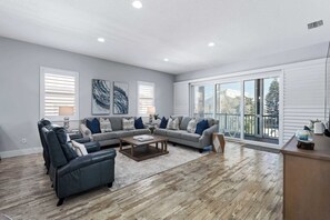 Ein geräumiges Wohnzimmer mit einer grauen Sofagarnitur, einem Couchtisch und einem großen Fenster mit Blick ins Freie.