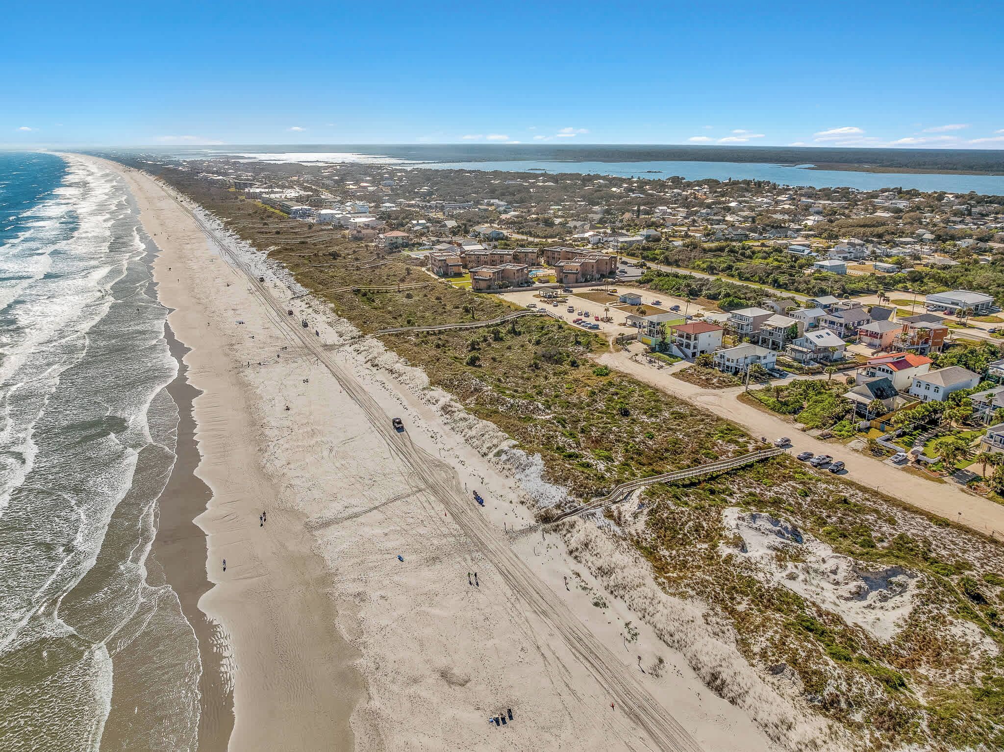 Vista aérea de un pueblo costero con playa, edificios residenciales y una carretera.