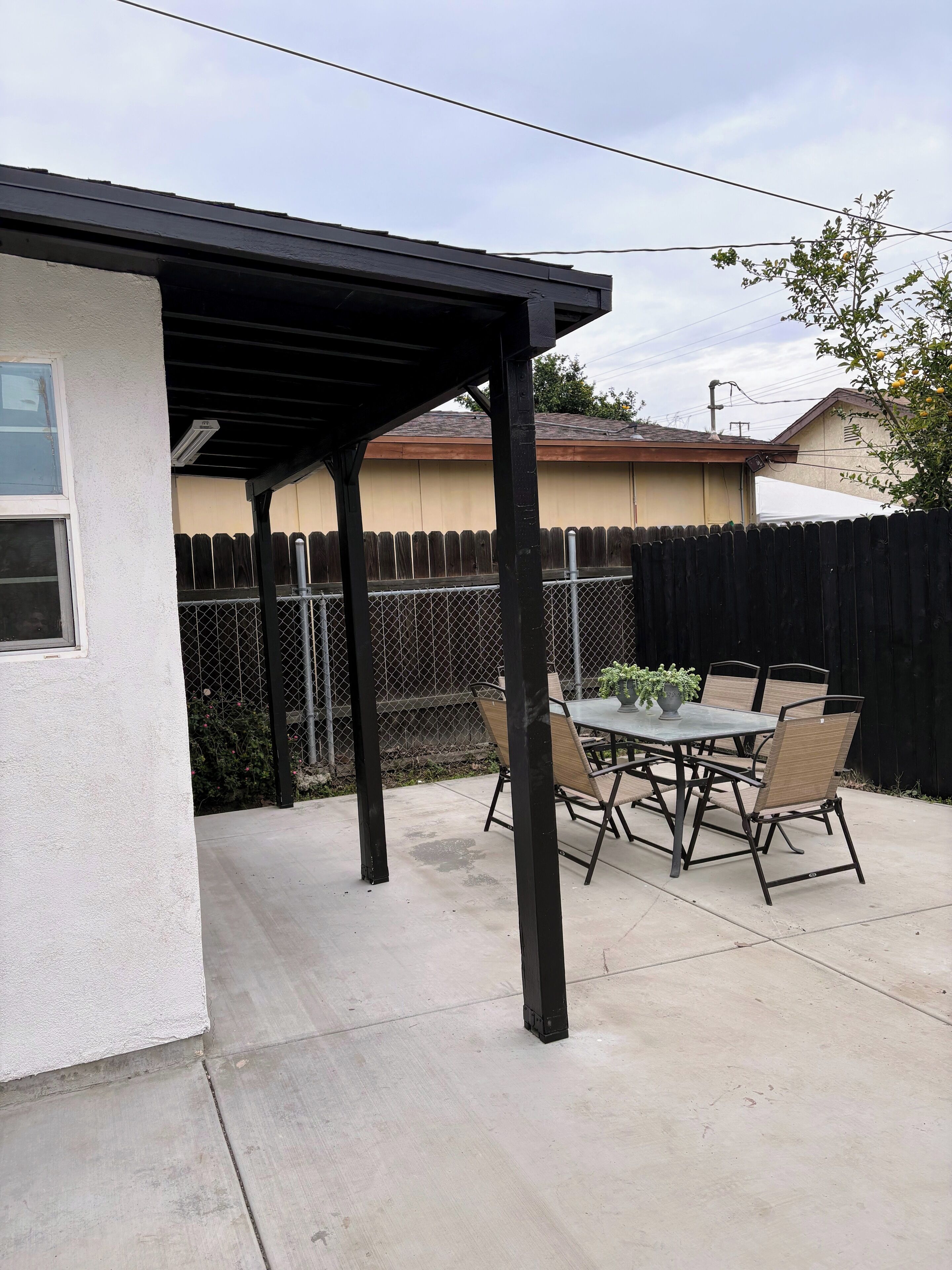 Un patio couvert avec une table et des chaises, une clôture et un bâtiment en arrière-plan.