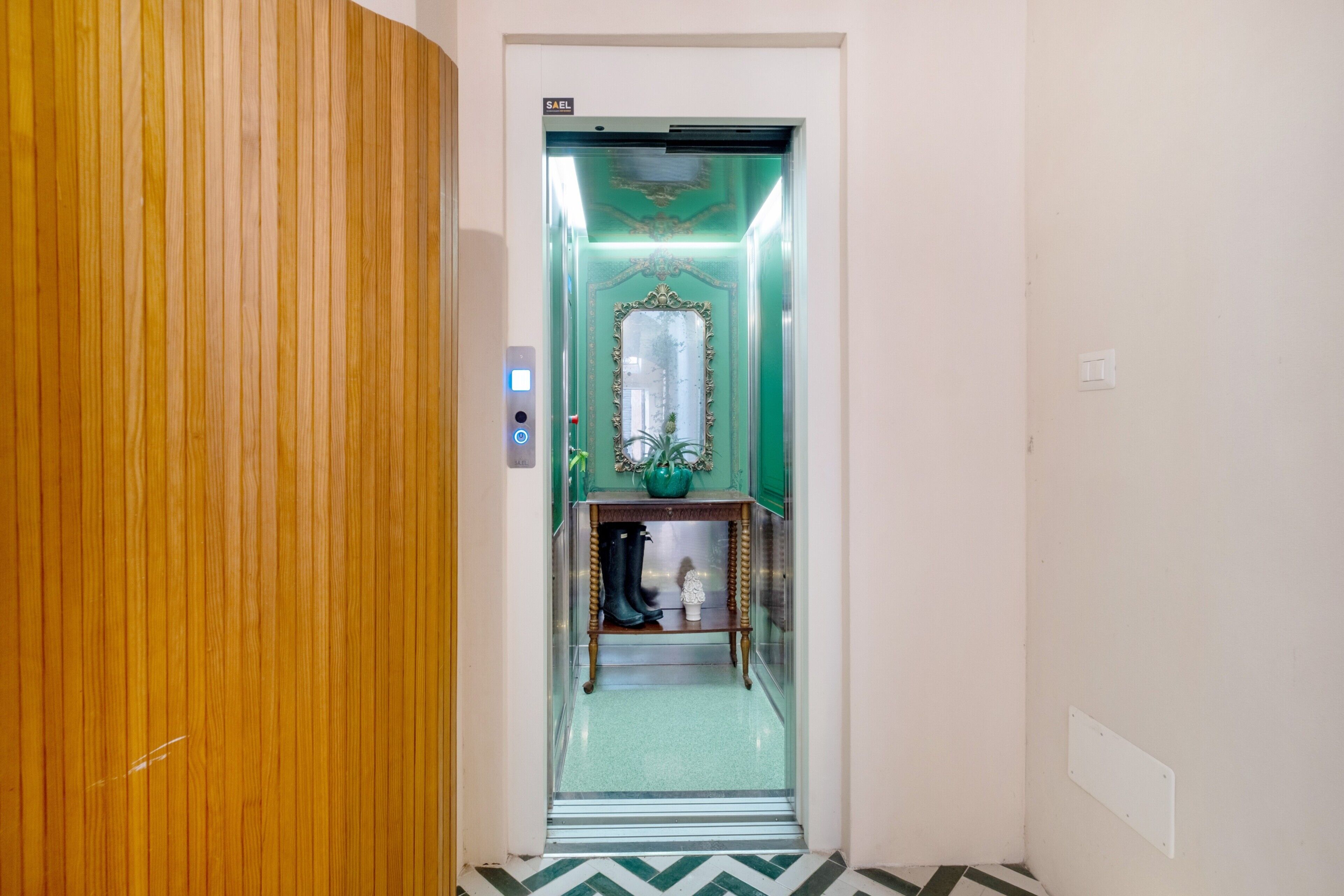 Un ascensor con un espejo, una mesa pequeña con una planta y una pared verde.