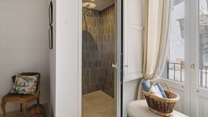 A bathroom with a shower, a chair, a wicker basket, and a window with curtains. - Room 'Nardo House: Matteotti Suite' with Shared Terrace, Wi-Fi and Air Conditioning (Nardò)
