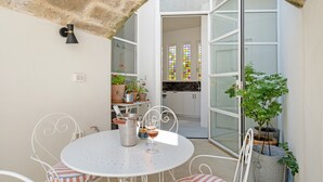 Eine Terrasse mit Tisch und Stühlen, einem Blumentopf und Blick in einen Küchenbereich mit einem Fenster.