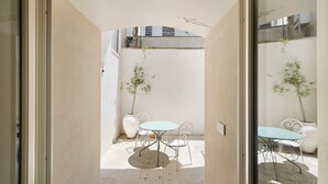 Una porta oberta que dona a un pati amb una taula, cadires, una planta en test i una paret de rajoles.