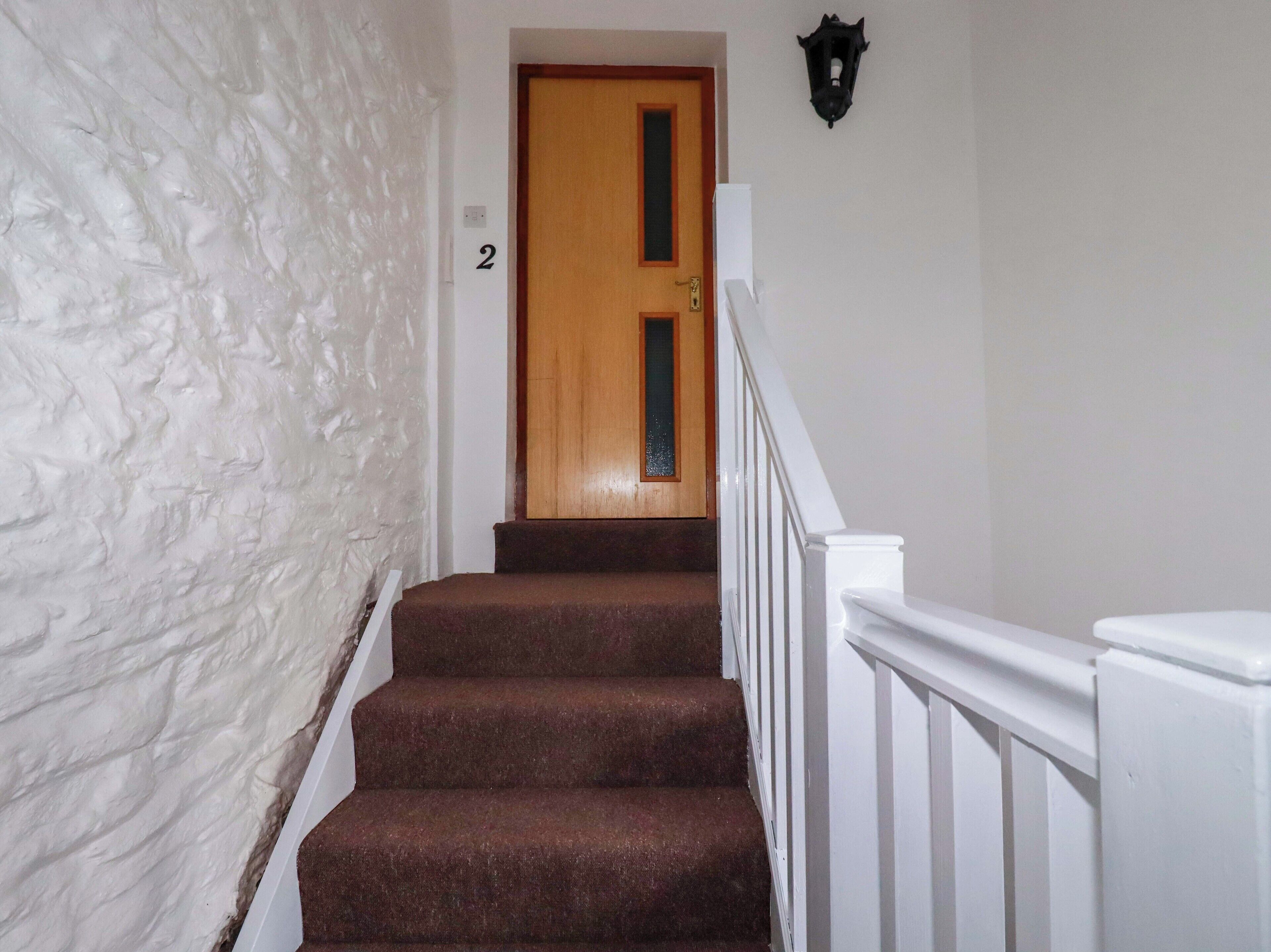 A staircase with a wooden door at the top, white walls, and a black wall-mounted light fixture.