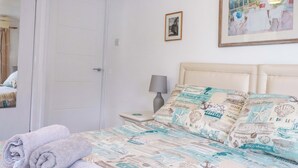 A bedroom with a bed, a nightstand, a lamp, and a door. - The Penthouse (Looe)