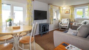 A cozy living room with a sofa, chairs, a TV, and a dining table with chairs. - The Penthouse (Looe)