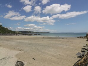 A wide sandy beach with a rocky shoreline, a clear blue sky, and distant hills. - The Penthouse (Looe)