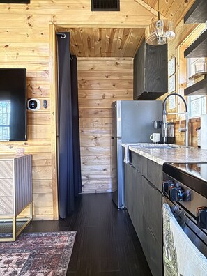 Eine kleine Küche mit Holzwänden, einem eingebauten Kühlschrank, einem Spülbecken und einem Fenster.