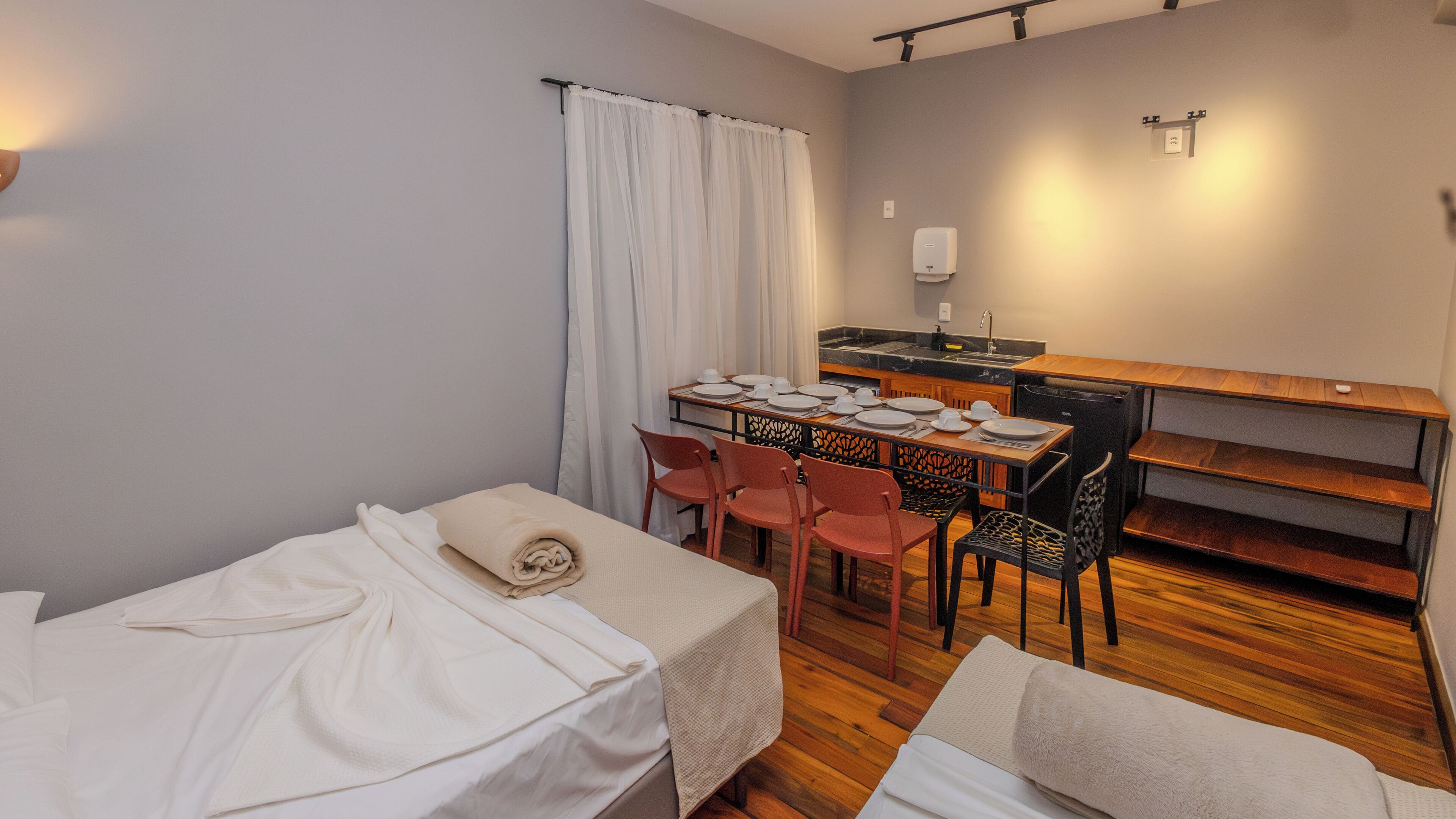 A small, compact room with a bed, a table set for dining, and a kitchenette.