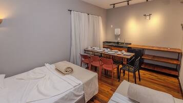 A small, compact room with a bed, a table set for dining, and a kitchenette.