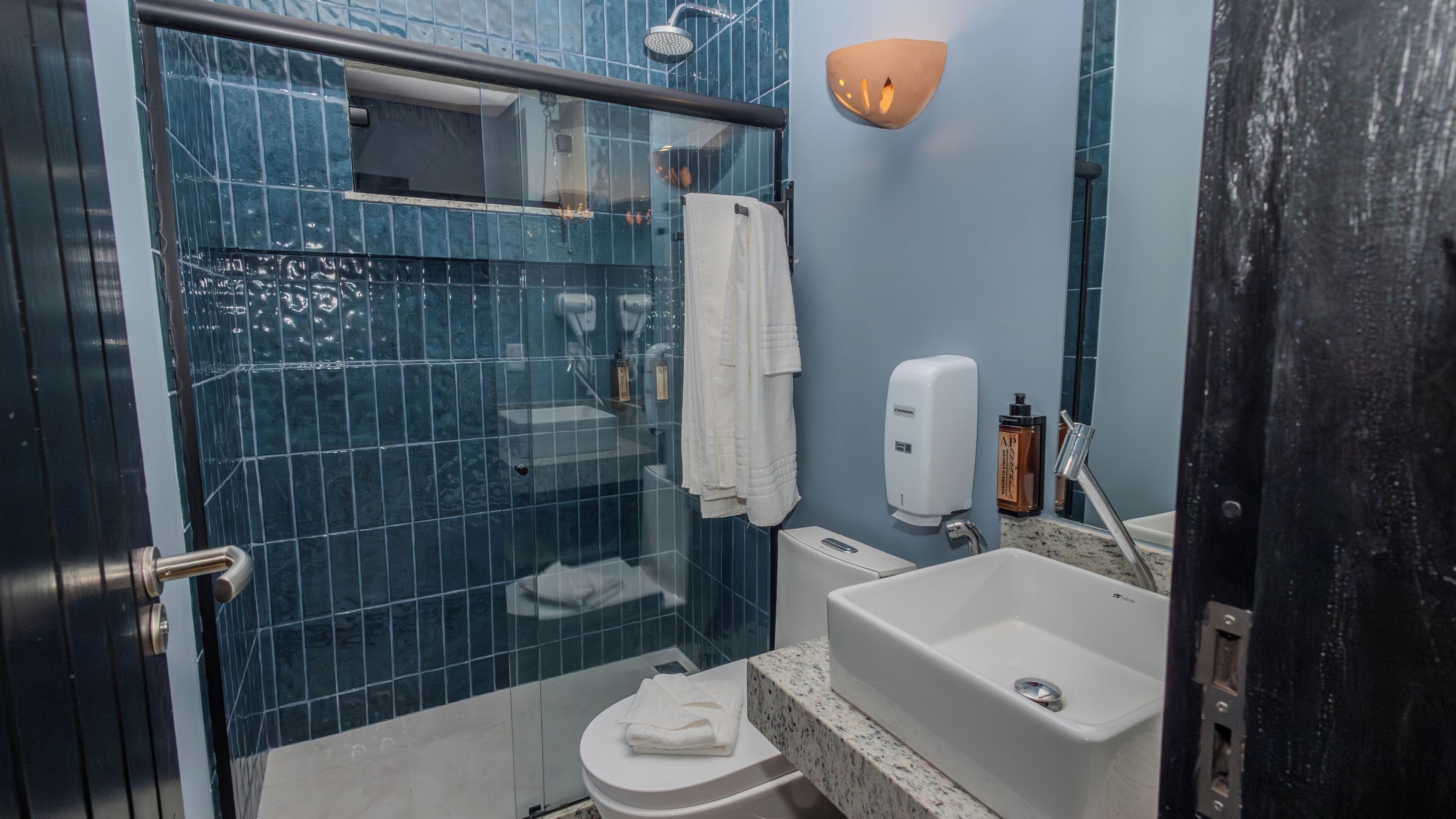 Un baño con cabina de ducha de vidrio, inodoro, lavamanos con dispensador de jabón y barra para toallas.