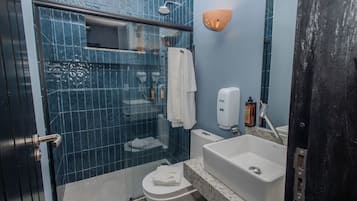 Un baño con cabina de ducha de vidrio, inodoro, lavamanos con dispensador de jabón y barra para toallas.