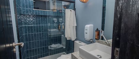 A bathroom with a glass shower enclosure, a toilet, a sink with a soap dispenser, and a towel rack.