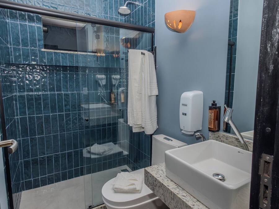Un baño con cabina de ducha de vidrio, inodoro, lavamanos con dispensador de jabón y barra para toallas.
