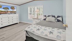 A bedroom with a bed, dresser, TV, and window with blinds. - Easy living lodge, large yard and parking area-heart of Murrells Inlet (Murrells Inlet)